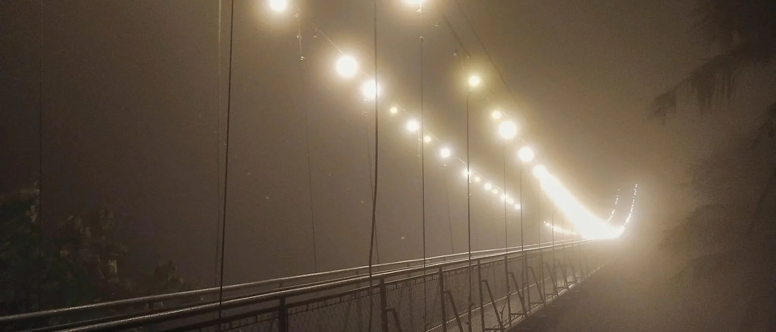 A lit suspension bridge running into fog