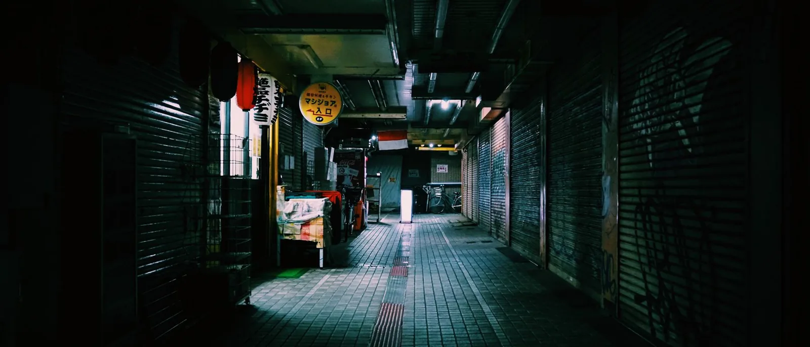 A night alley of closed shutters, one light on
