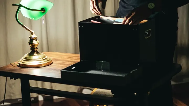 A silhouette working at a laptop by lamplight