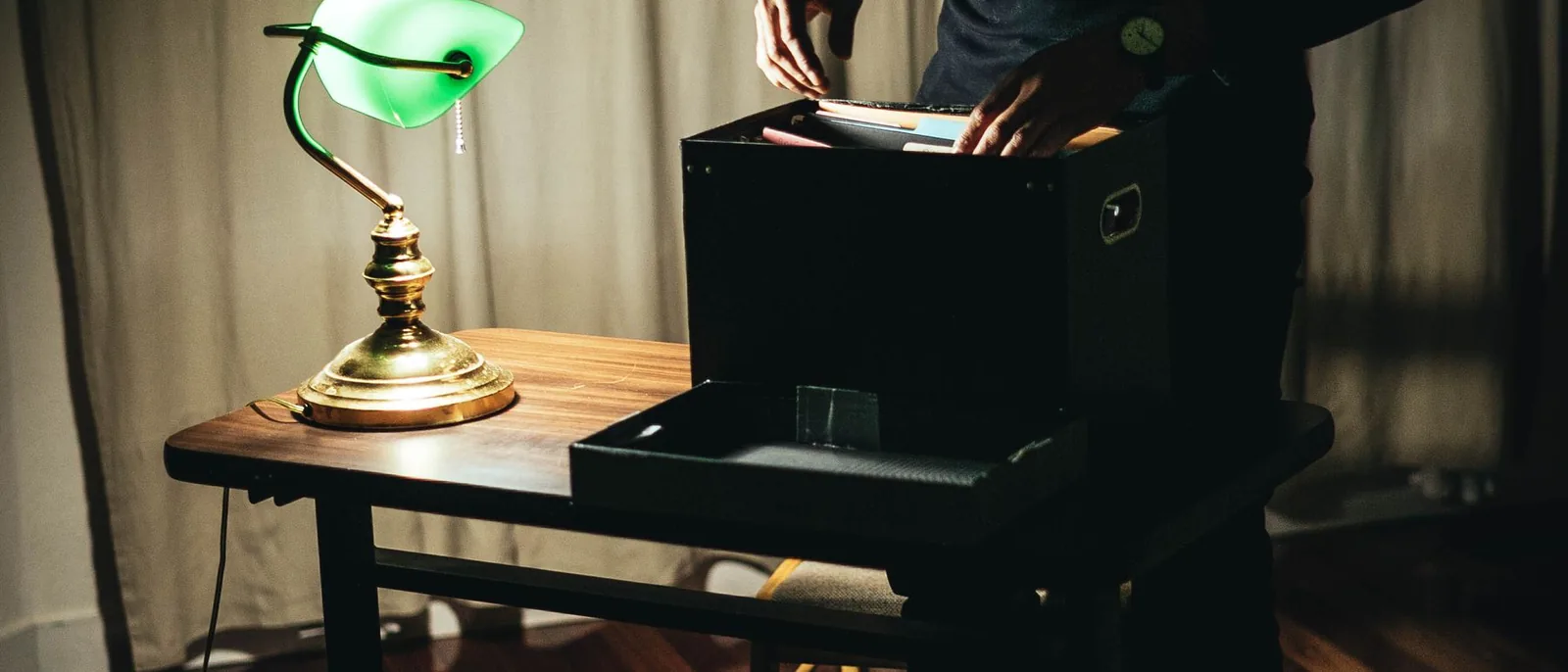 A silhouette working at a laptop by lamplight