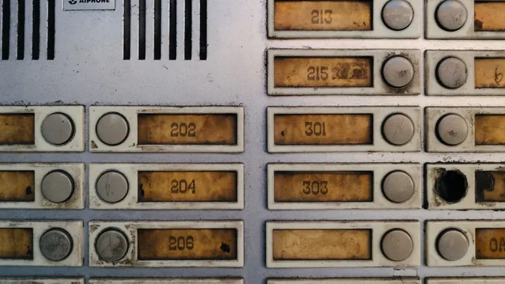 A worn intercom panel with labelled buttons